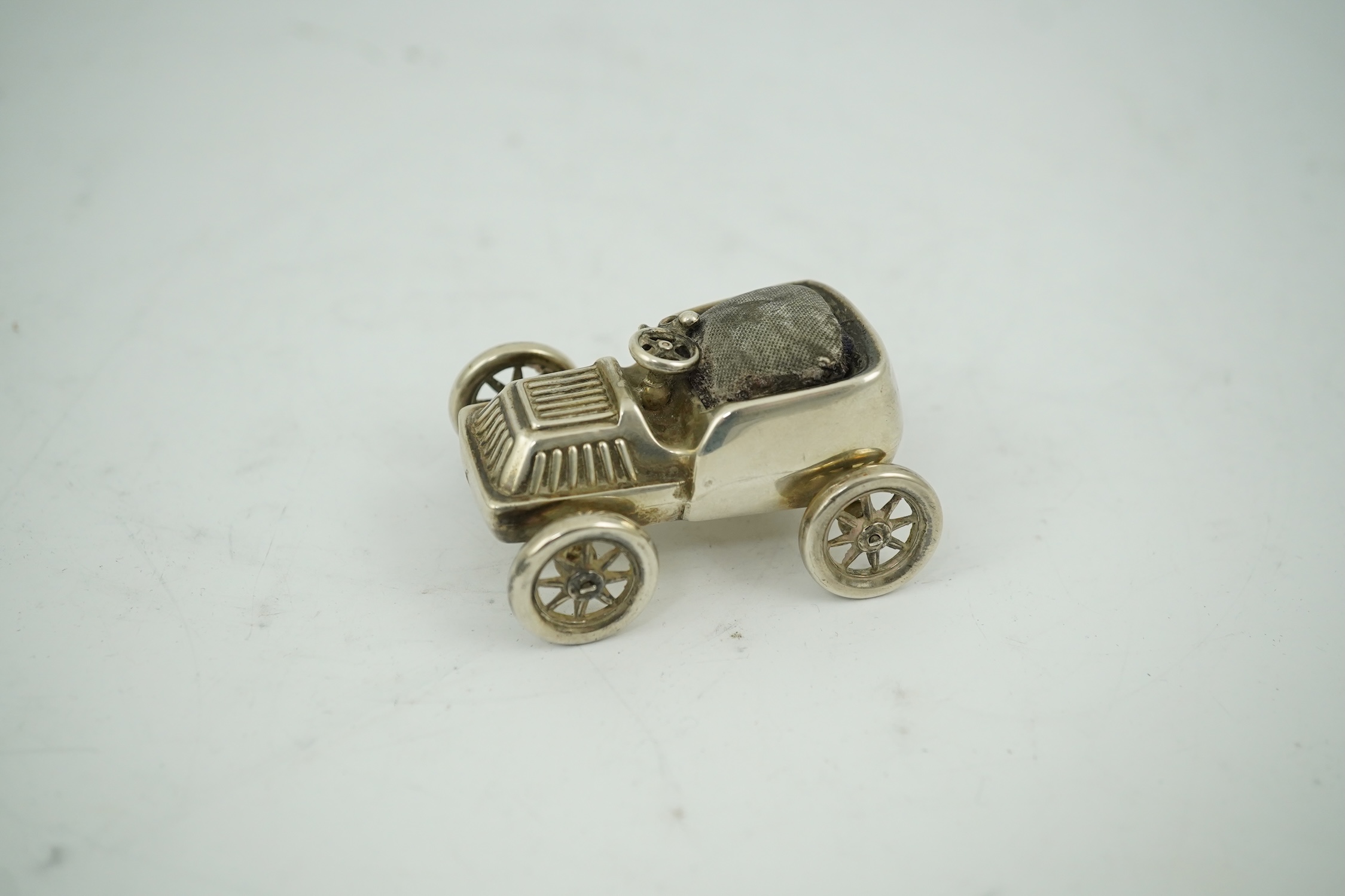 An Edwardian novelty silver mounted pin cushion modelled as a vintage car, makers mark rubbed, Birmingham, 1906, 57mm. Condition - poor to fair